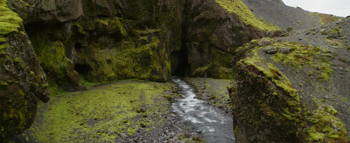 People walk near a river flowing into a cave