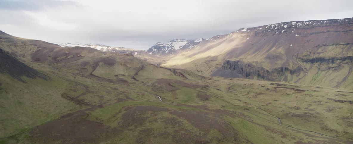 Green mountains with some snow covered tops on a cloudy day