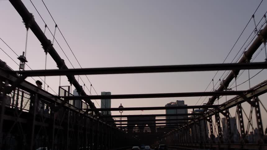 Vehicles cross a bridge into a city at dawn