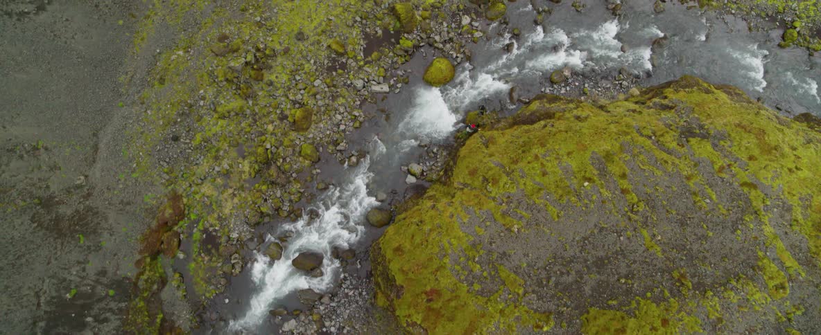 Two people are hiking along a fast running stream during the day