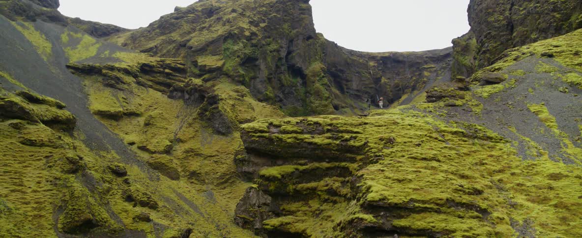 Two people stand on a cliff watching a river is flowing rapidly through a mountain ravine during the day