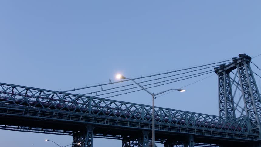 Street lights shine below a suspension bridge in a city at dusk