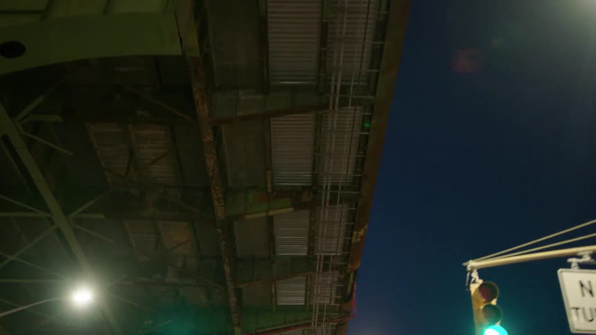 A vehicle drives beneath a city bridge at night