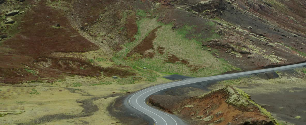 A road is winding through the tundra in a natural landscape during the day