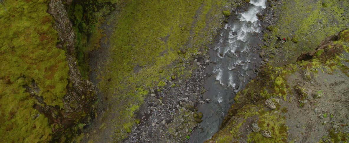 Two people are hiking along a fast running stream during the day