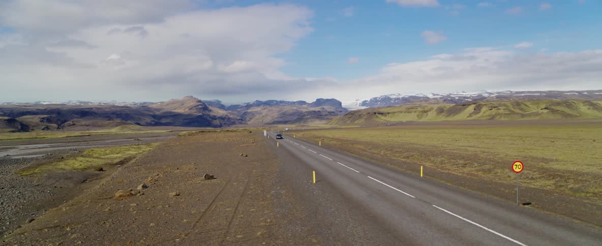 A black car travels down a long lonely highway