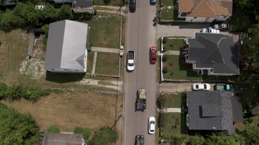 Military trucks follow a police car on a neighborhood road