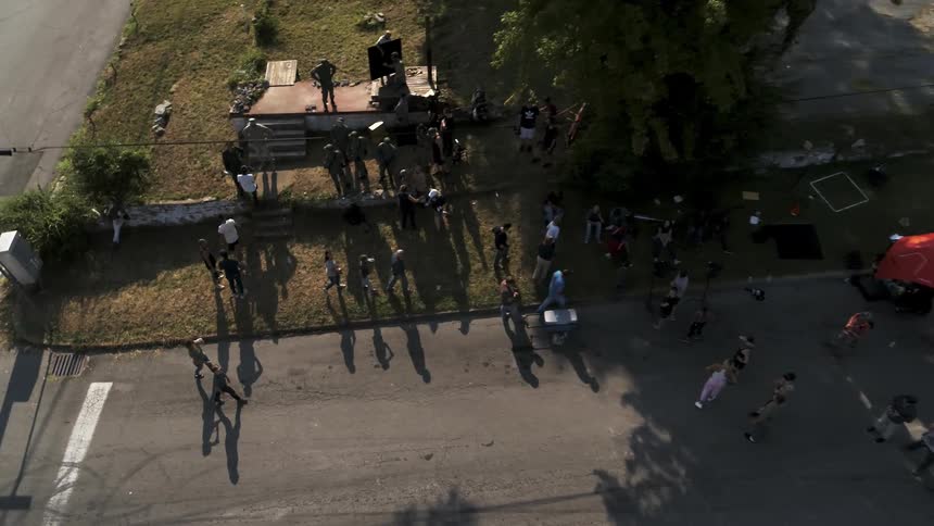 A  group of people mills about on a vacant lot in a town during the day