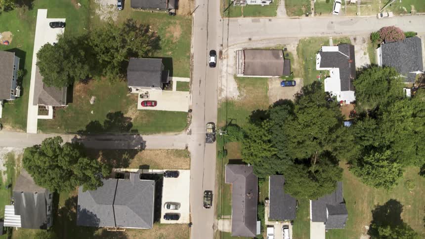 Convoy of cars drive through a neighborhood on a sunny day