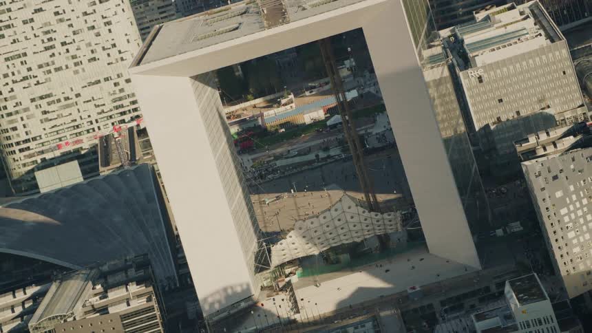 The sun is casting light and shadow on an open square building in a city during the day