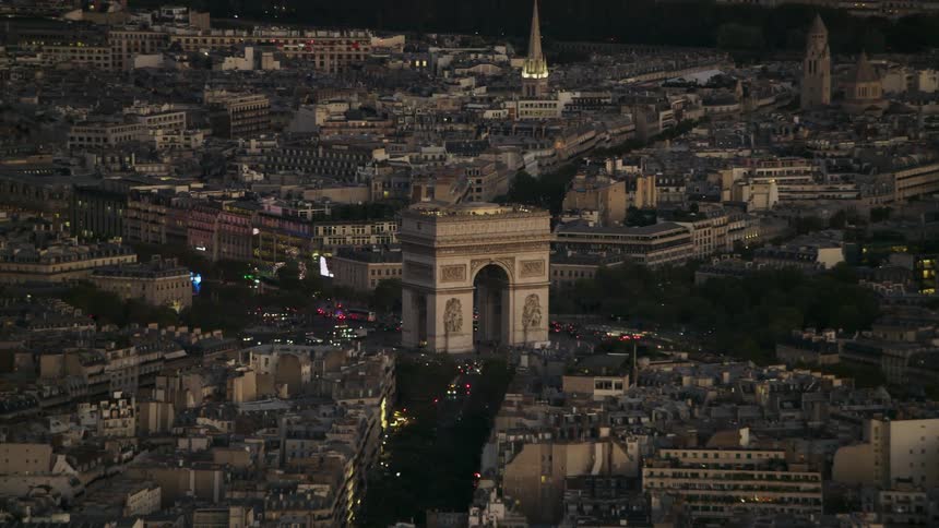 Traffic travels on streets near a monumental arch at dusk