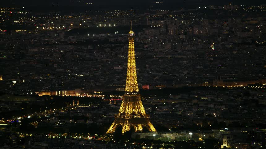 The eiffel tower is lit up at night with a rotating spot light on top