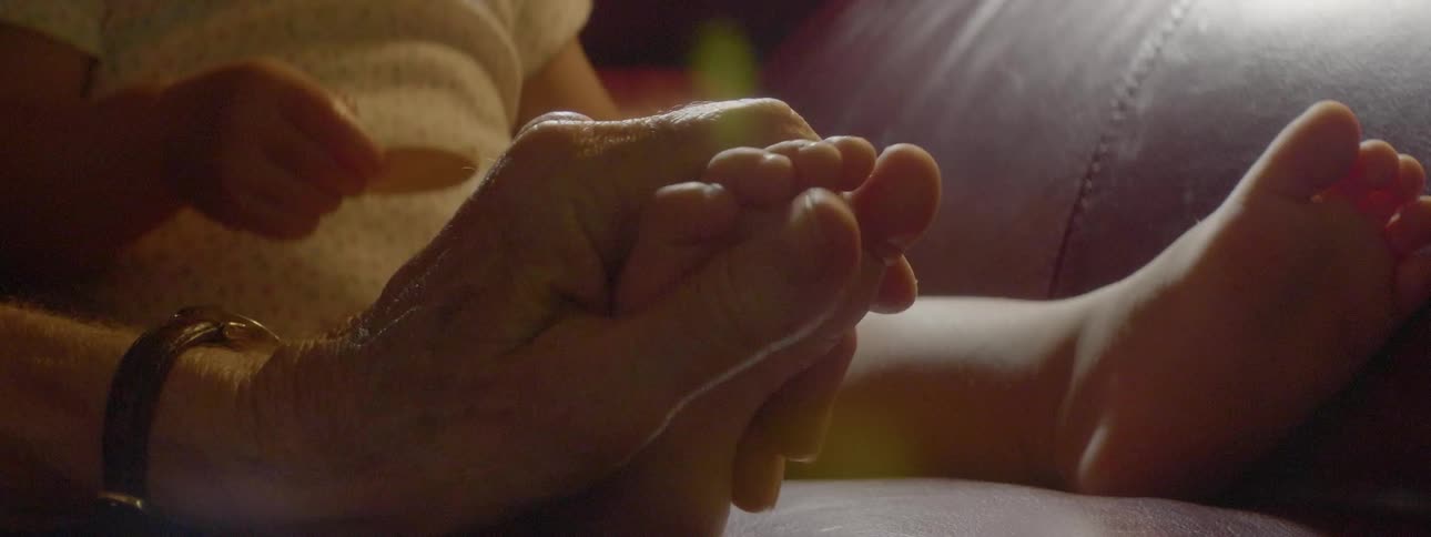 An old person is rubbing a baby's hand during the day