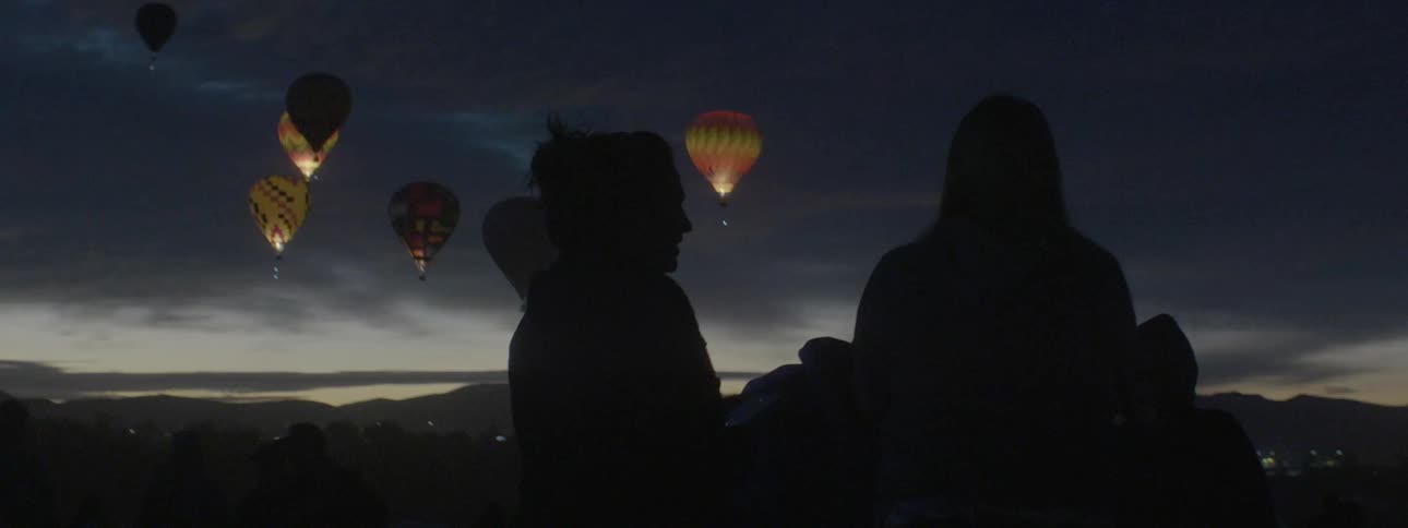 People watch flickering hot air balloons in the night sky