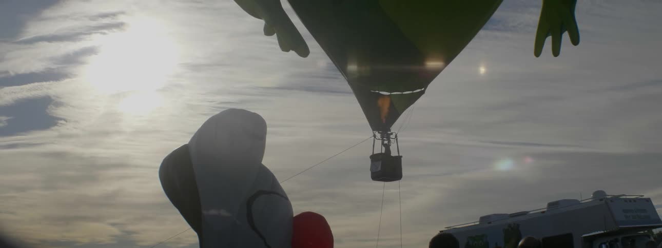 A pilot is landing a hot air balloon tethered by ropes at dusk