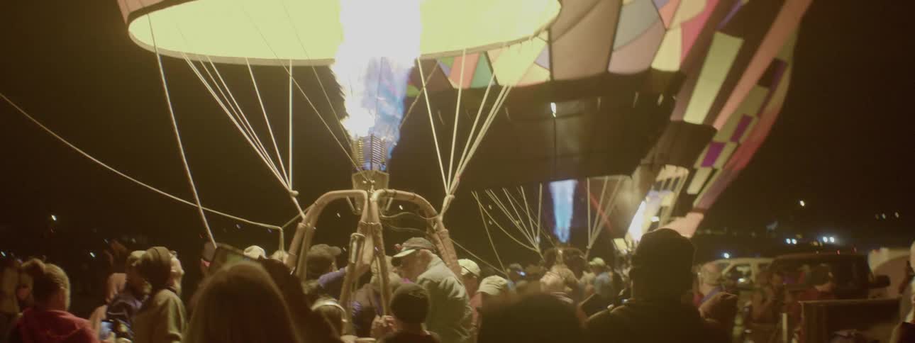 People stand around hot air balloons at night