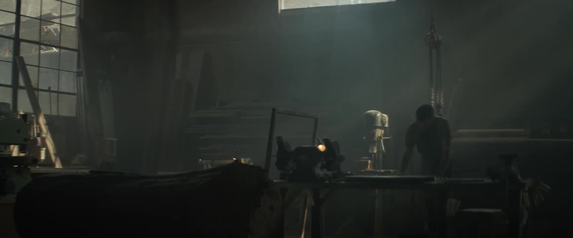 The man is leaning over his workbench