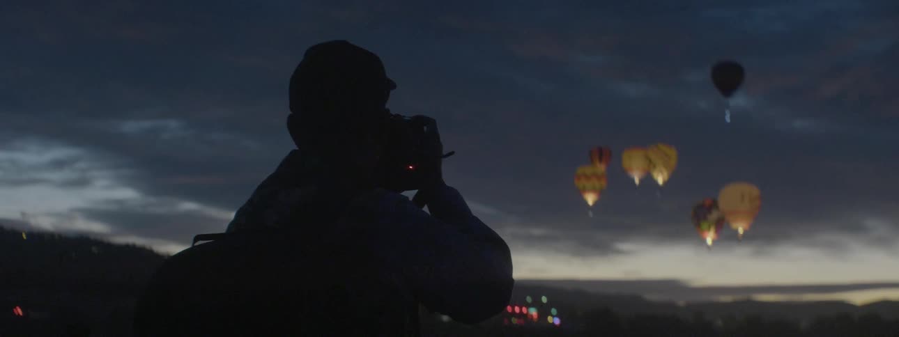 A man films flickering hot air balloons in the sky