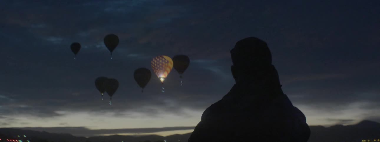 A man watches flickering hot air balloons in the sky