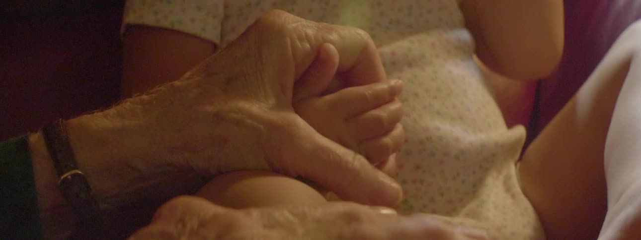 An older man is holding the hand of a young baby
