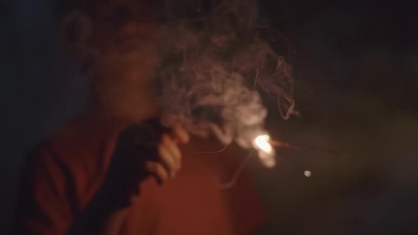 A man in a reddish shirt is holding a sparkler as it burns