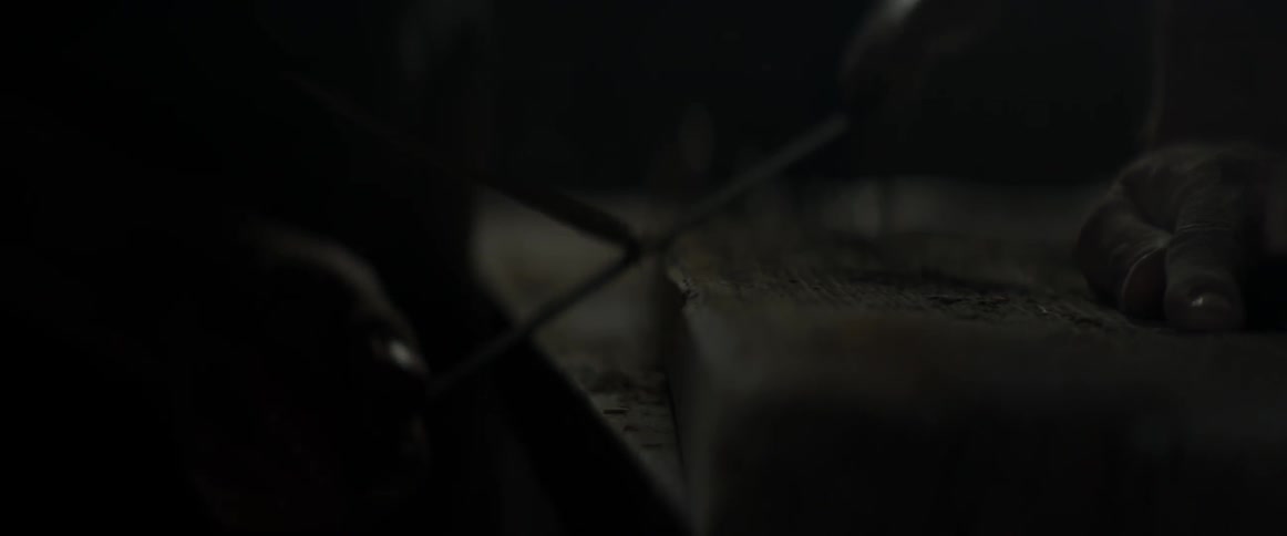 A person shaves a plank of wood in the dark