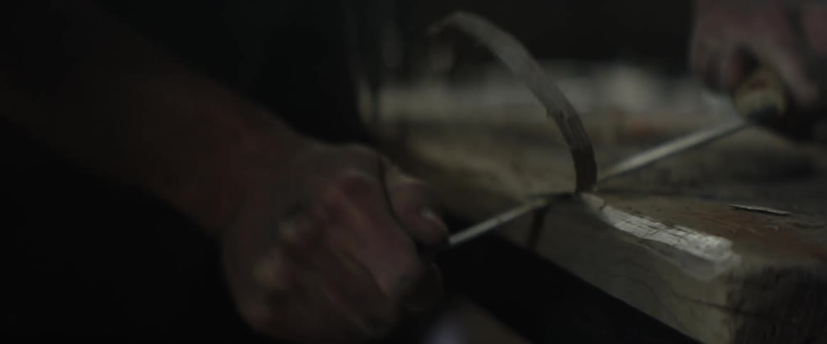 A man shaves wood with a large blade