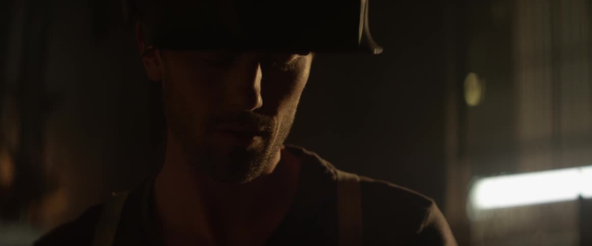 A man wears a welding mask on his head in a dark workshop