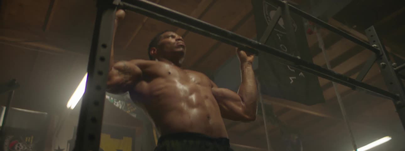 An athlete is doing pull ups in a gym during the day