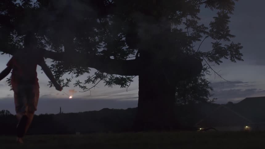 A white teenager spins around in a park while holding fireworks