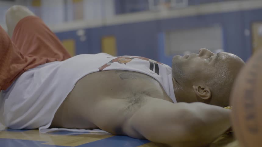 A black man lies on a basketball court and breathes