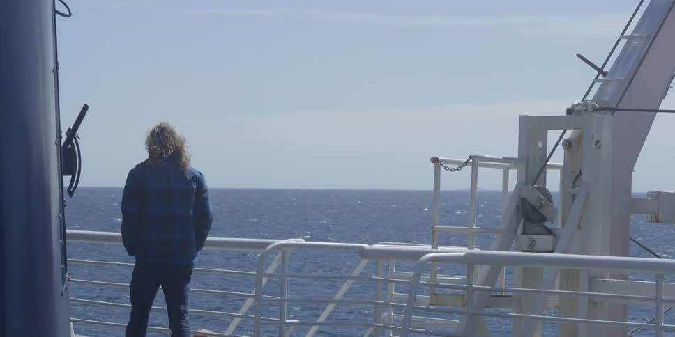 A man is walking along the railing of ship at sea on a sunny day