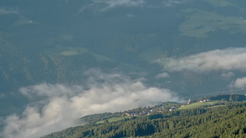 Fog and clouds are drifting over a mountain village during the day
