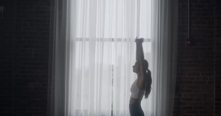 A woman stretches in front of a window