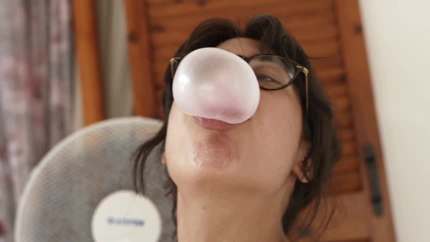 A girl with glasses on is blowing bubble gum