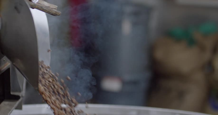 Coffee beans are poured through a funnel into a vat