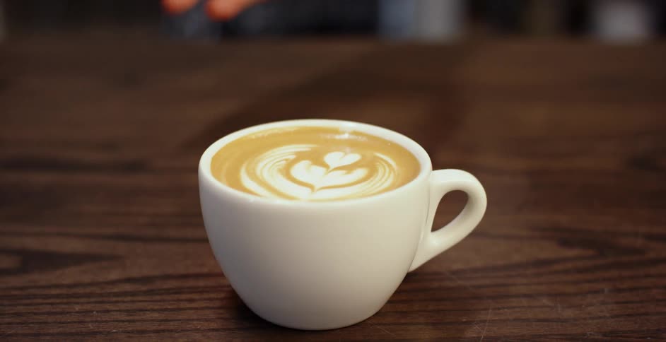 A hand slides a latte across a wood table