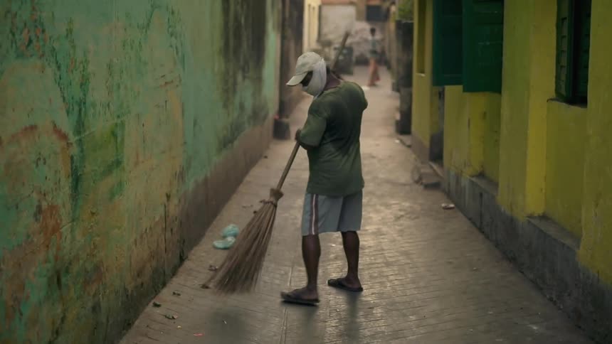 A man in a green shirt sweeps an alleyway