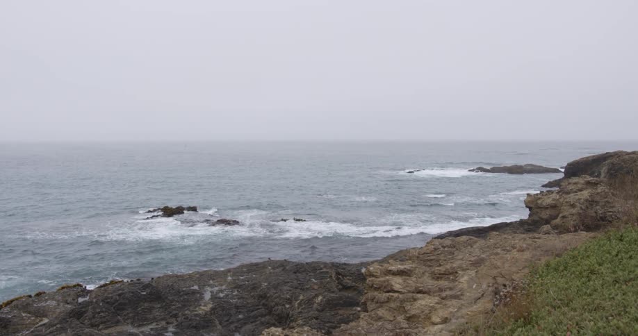 The waves are crashing against the shore on a foggy day