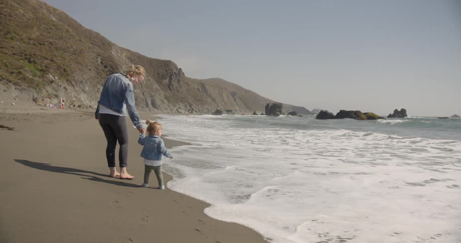 A woman walks a young girl on the beach by the water