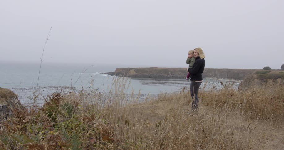 A woman holds a baby by the shore