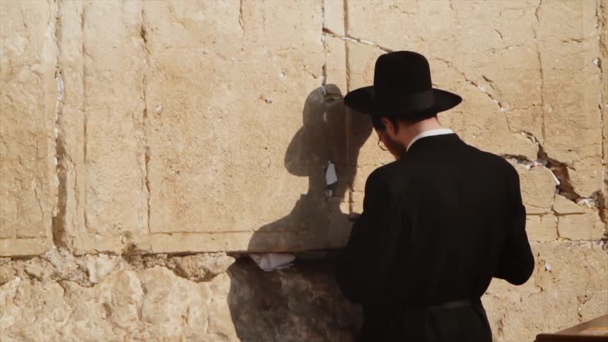A man stands close to the stone giving off a shadow