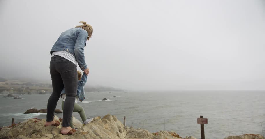 A mother and child are standing at the edge of a cliff overlooking the ocean