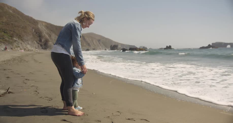A woman is holding a child's hands by the water
