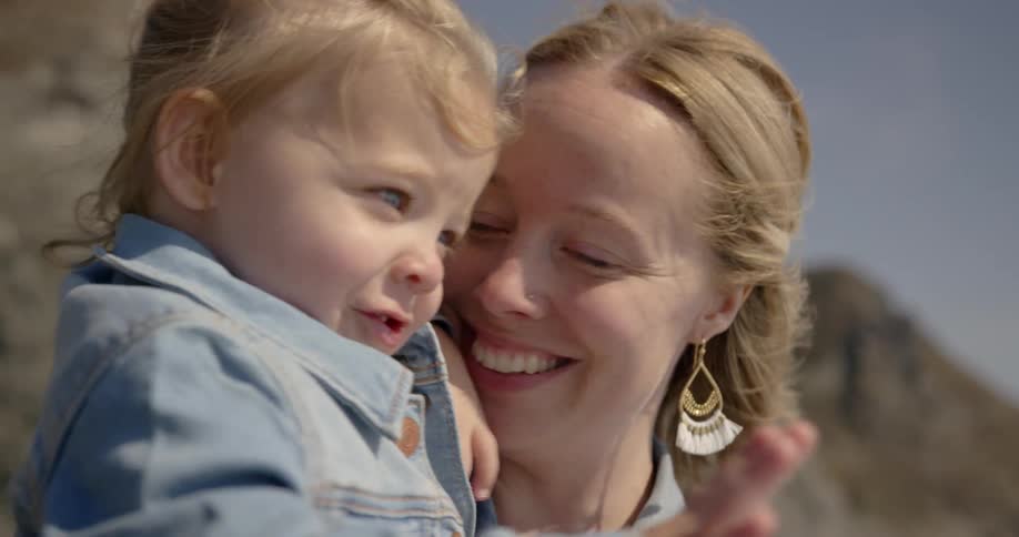 A woman smiles while holding a toddler on a sunny day