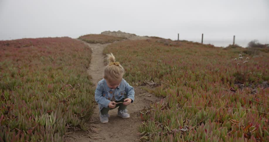 A child squats on a dirt path and looks at a stick