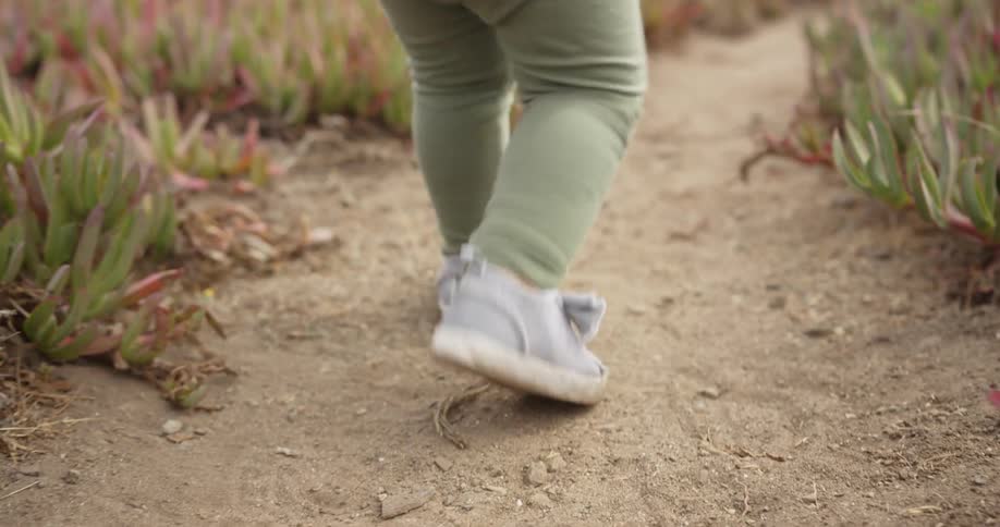 Toddler takes small steps along a sandy path