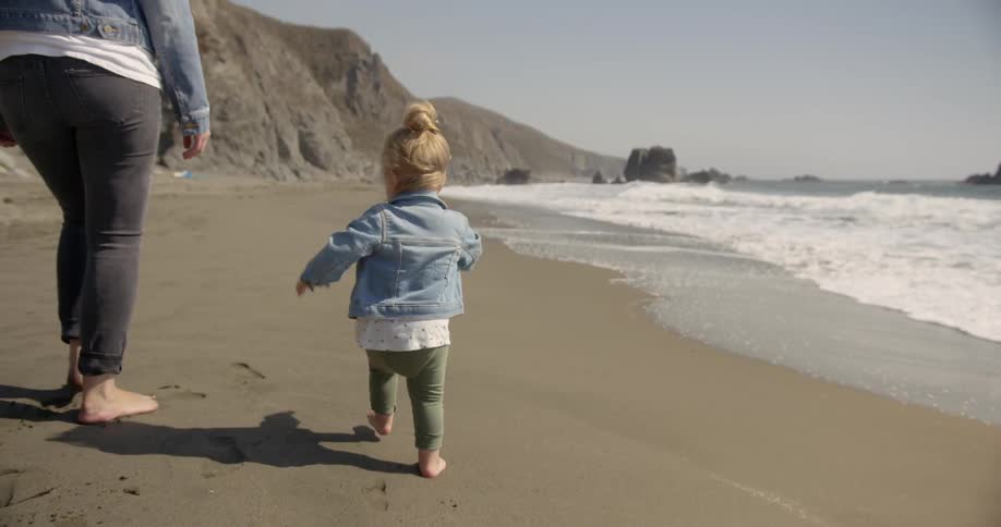 A woman and child walk together on the beach