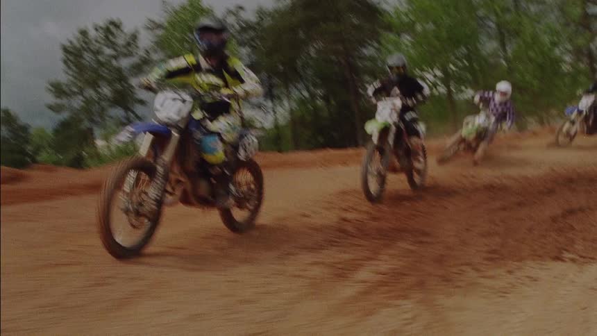 A large group of people are racing dirt bikes around a track