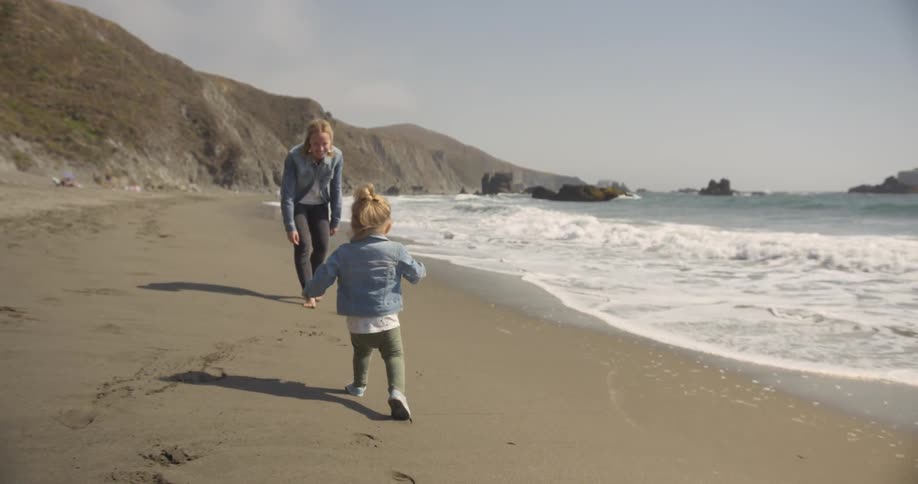 A small child and a woman are playing on the beach